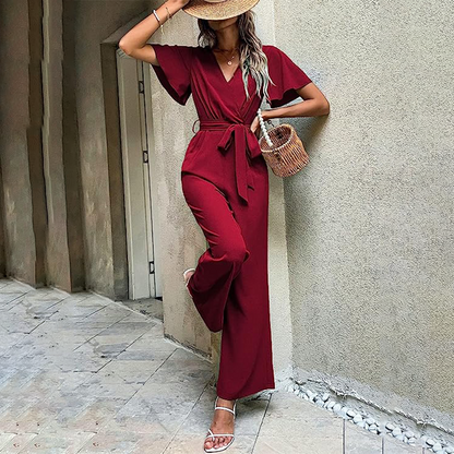 Donna in tuta rossa elegante, cappello di paglia, borsa intrecciata, sandali bianchi. Moda estiva, abbigliamento casual chic, stile urbano.