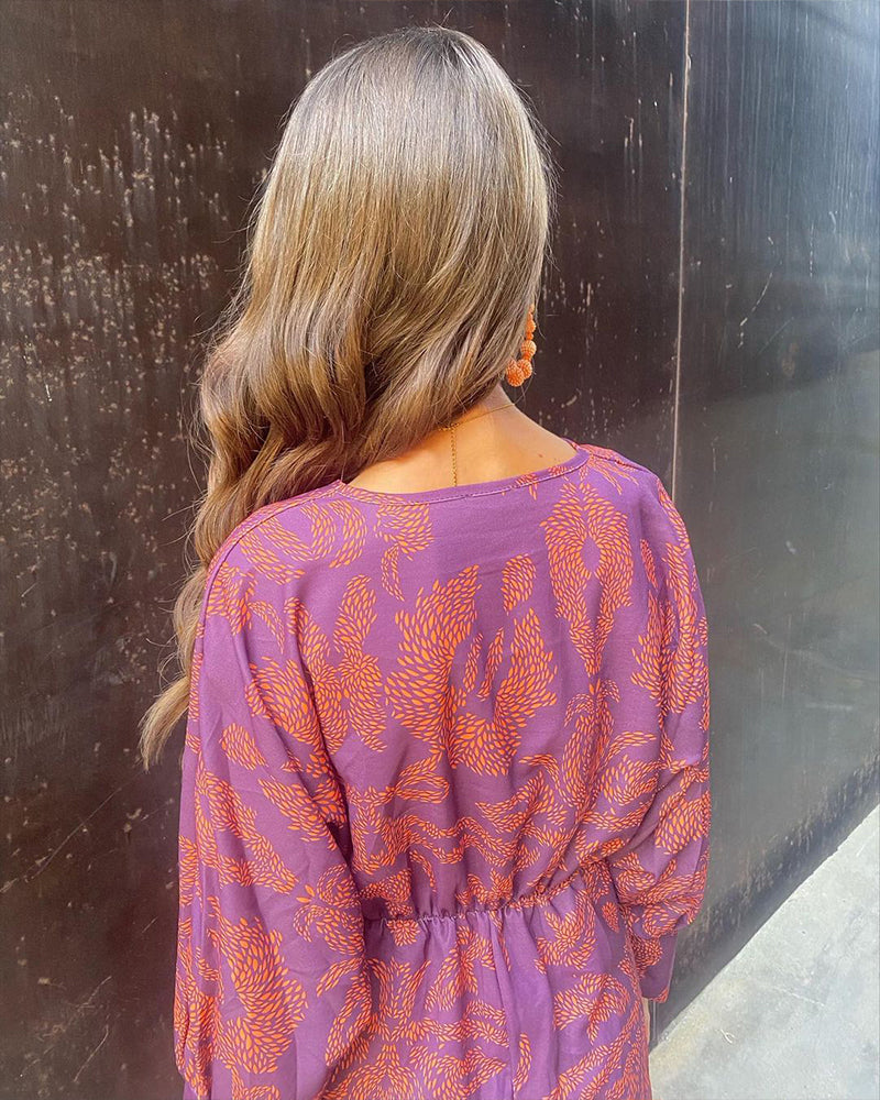 Donna di spalle con capelli ondulati, indossa abito viola con motivi arancioni. Moda autunnale, stile elegante, tendenze capelli 2023.