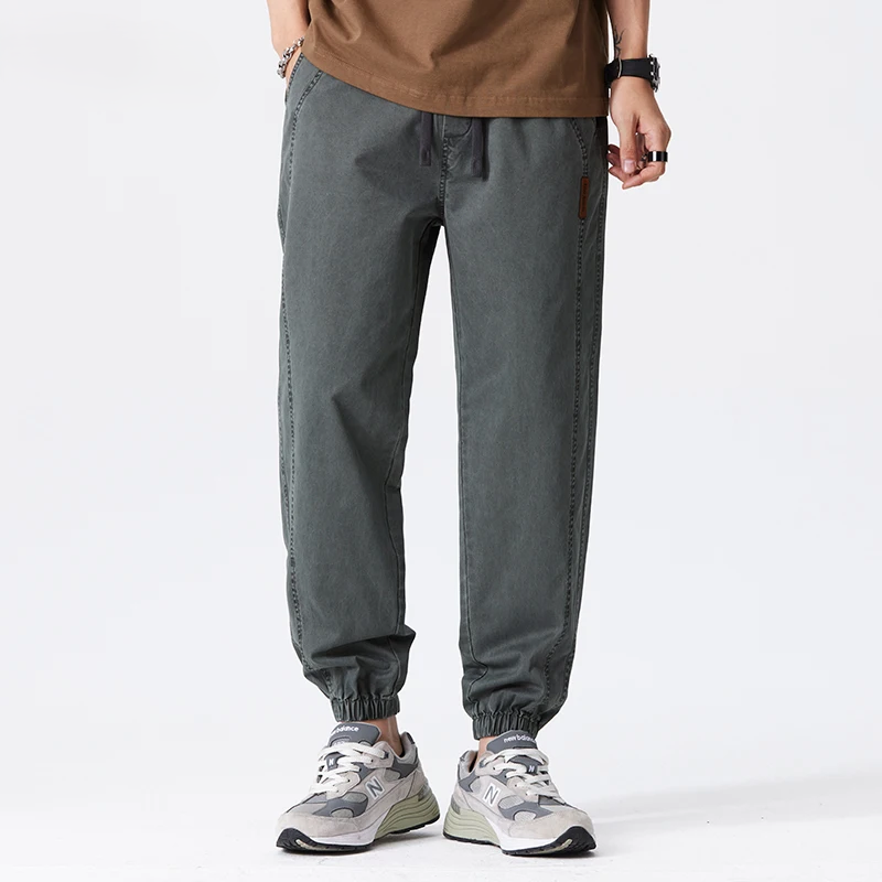 Pantaloni jogger grigi da uomo, stile casual, con elastico alla caviglia, abbinati a scarpe sportive bianche e grigie, moda streetwear.