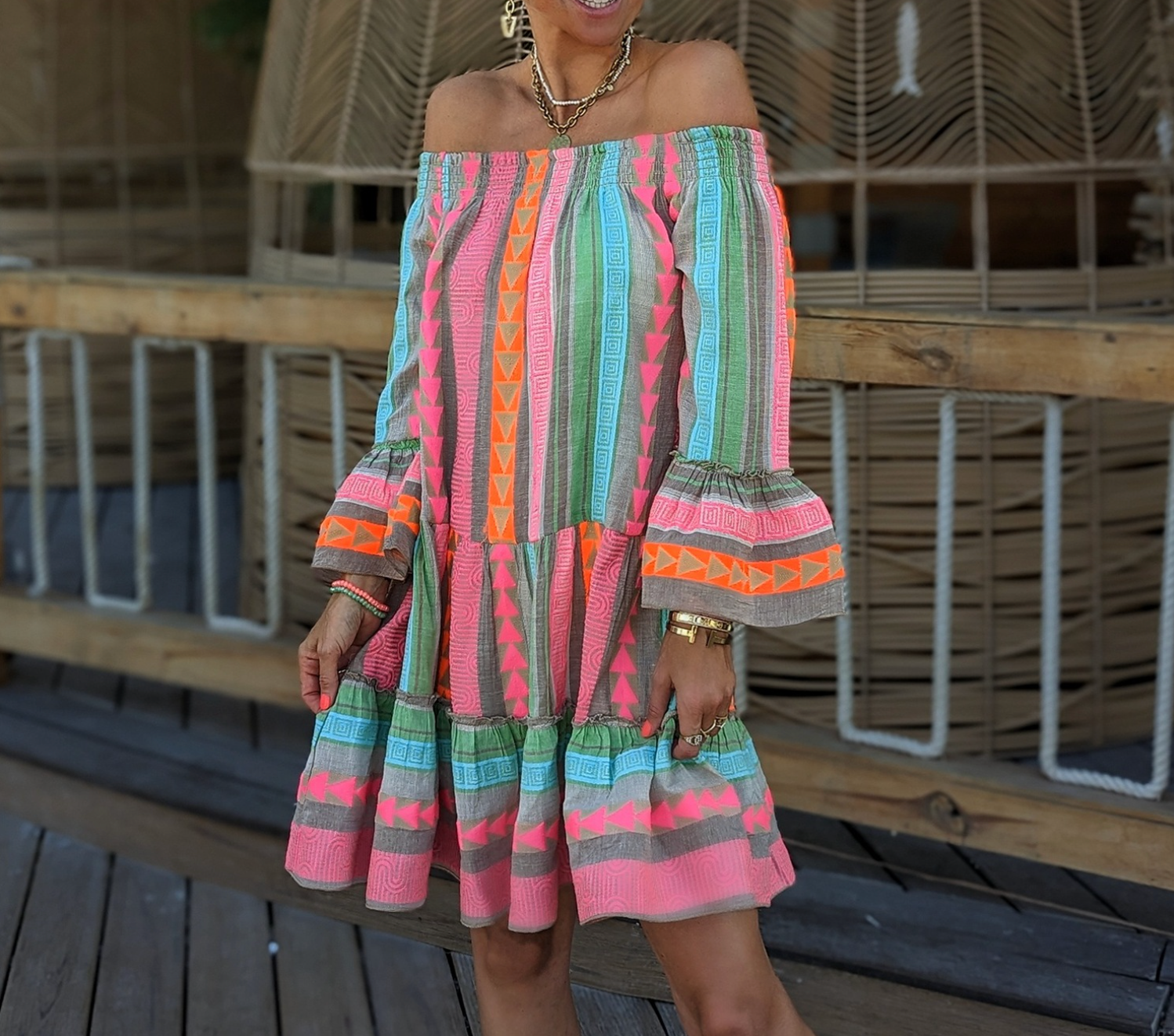 Abito estivo colorato a spalle scoperte con motivi geometrici, indossato da una donna su una passerella in legno. Moda estiva, abbigliamento femminile.