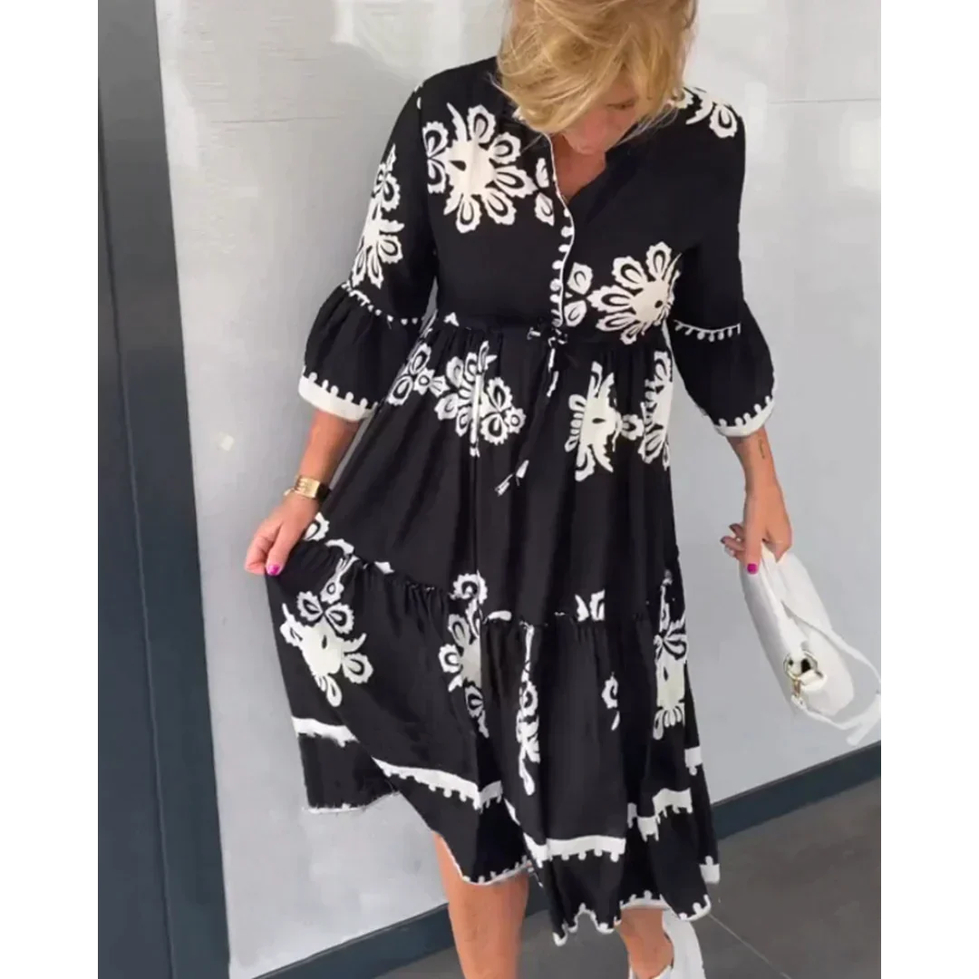 Abito nero con motivi floreali bianchi, maniche a tre quarti, indossato da una donna con borsa bianca. Moda elegante, abbigliamento femminile casual.