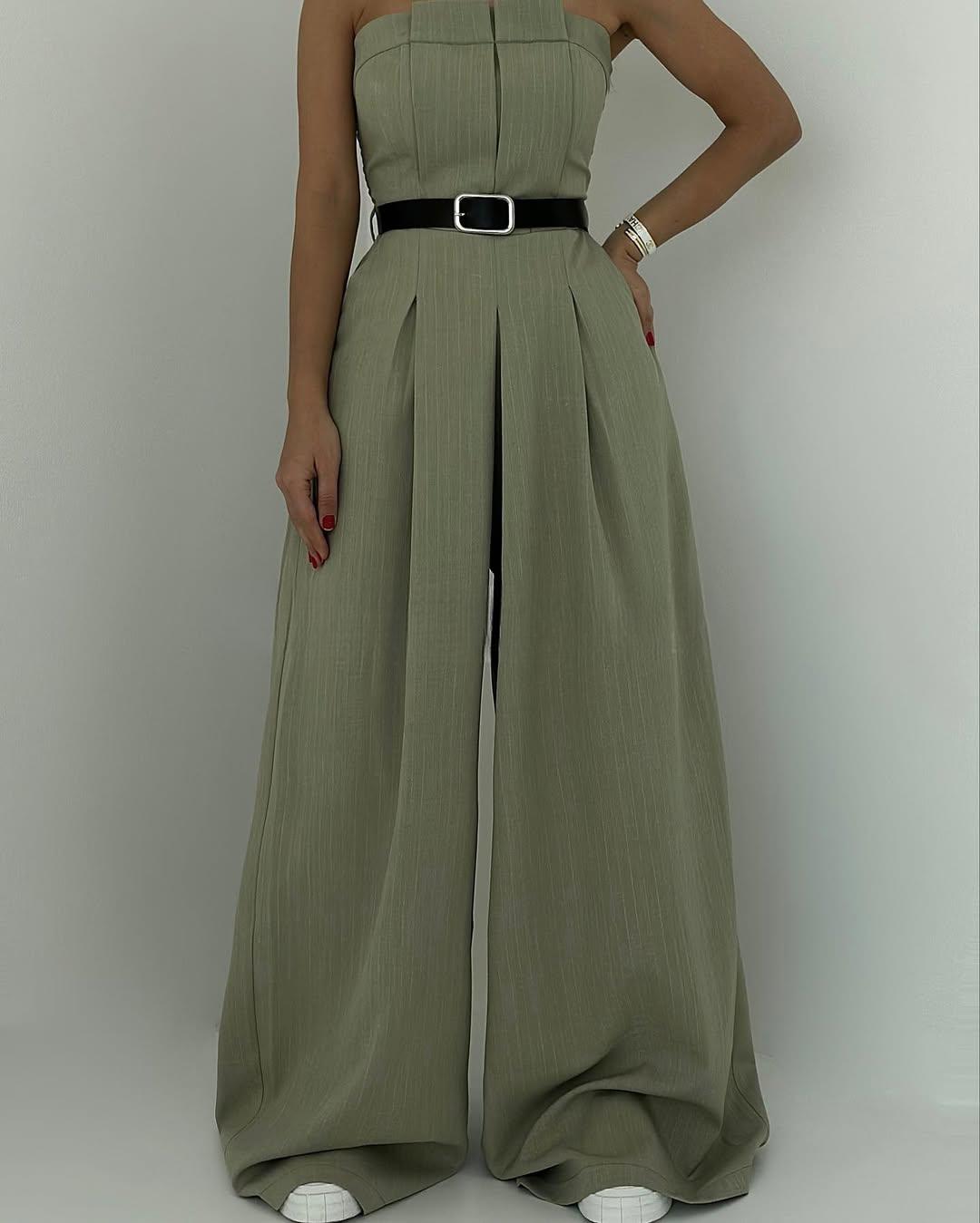 Donna in elegante tuta verde oliva con cintura nera, pantaloni a palazzo e scarpe bianche. Moda femminile, abbigliamento chic, stile contemporaneo.