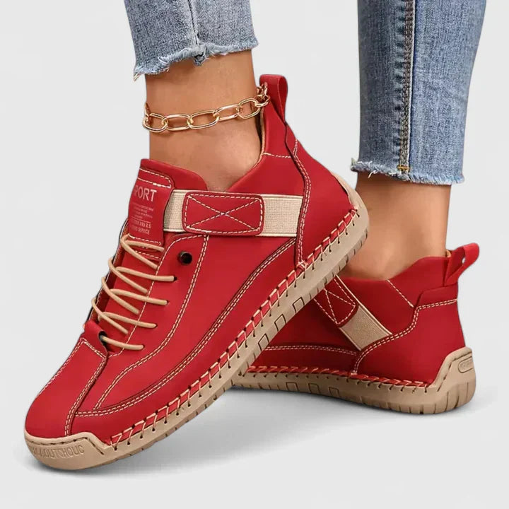 Scarpe sportive rosse da donna, design moderno con suola in gomma beige, indossate con jeans aderenti e cavigliera a catena dorata.