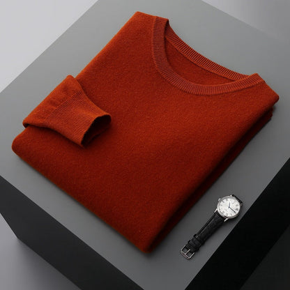 Maglione arancione piegato su tavolo grigio con orologio da polso nero e quadrante bianco. Moda autunnale, abbigliamento elegante, accessori uomo.