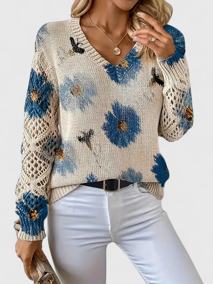 Maglione donna beige con fiori blu, lavorato a maglia, maniche traforate, abbinato a pantaloni bianchi. Moda autunnale elegante e casual.