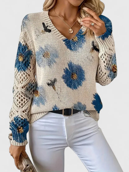Maglione donna beige con fiori blu, lavorato a maglia, maniche traforate, abbinato a pantaloni bianchi. Moda autunnale elegante e casual.