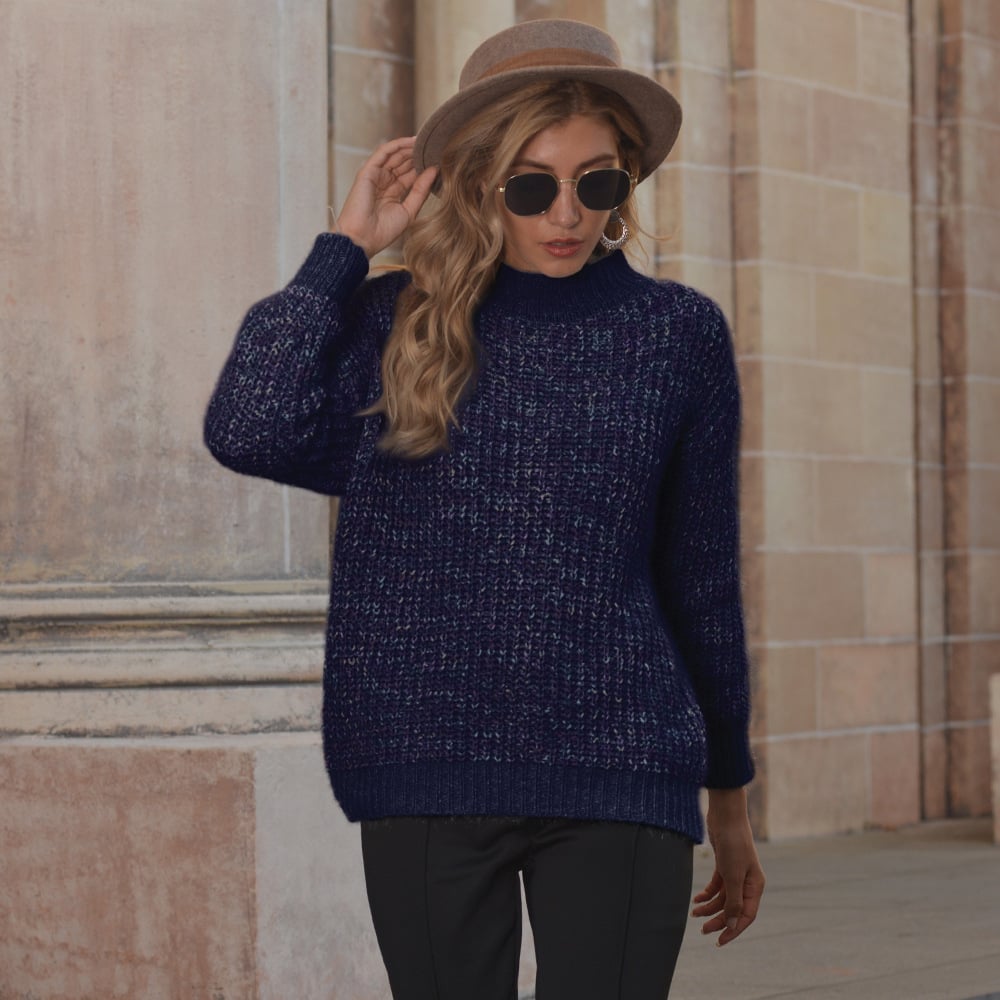 Donna con maglione blu scuro, cappello marrone e occhiali da sole, cammina davanti a un edificio storico. Moda autunnale, stile urbano elegante.