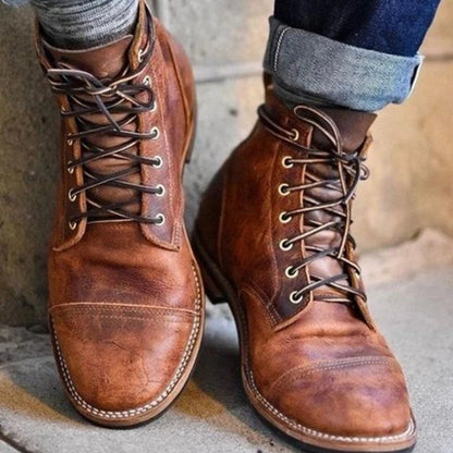 Stivali in pelle marrone da uomo, stile vintage, con lacci e cuciture a vista, indossati con jeans arrotolati. Scarpe eleganti e robuste.