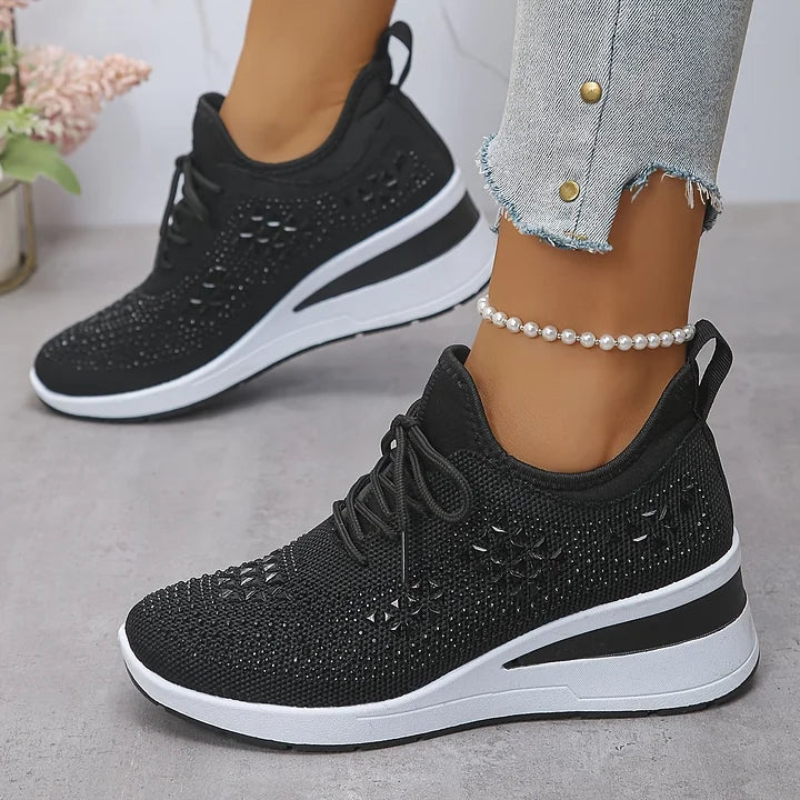 Scarpe da ginnastica nere con zeppa, dettagli traforati, suola bianca, indossate con jeans strappati e cavigliera di perle. Moda casual donna.