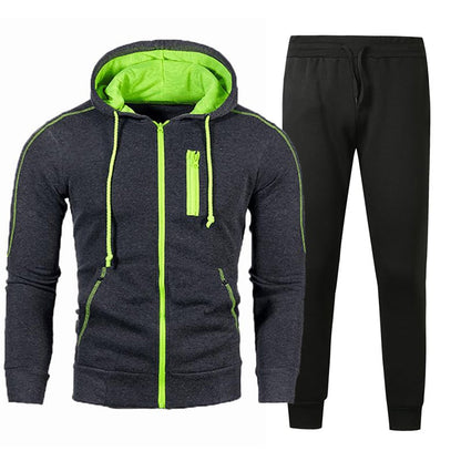 Tuta sportiva uomo, felpa con cappuccio grigio scuro e dettagli verdi, pantaloni neri. Abbigliamento casual, moda fitness, stile moderno.