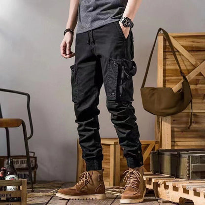 Pantaloni cargo neri da uomo con tasche multiple, abbinati a stivali marroni su pavimento in legno. Moda casual maschile, abbigliamento urbano.