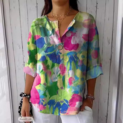 Camicia donna floreale colorata, maniche a tre quarti, sfondo bianco, bottoni decorativi, moda estiva casual, stile vivace e moderno.