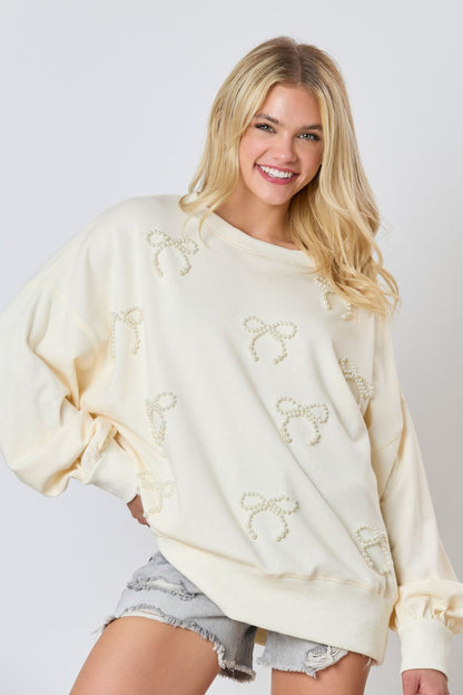 Donna sorridente con maglione bianco decorato con perle, indossa shorts di jeans. Moda casual femminile, abbigliamento autunnale trendy.