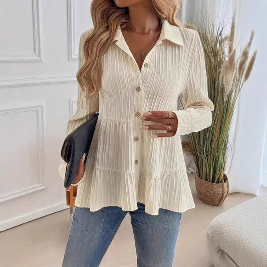 Donna con camicia bianca a coste, jeans blu, borsa nera, in un interno moderno con piante decorative. Moda casual elegante, stile autunnale.