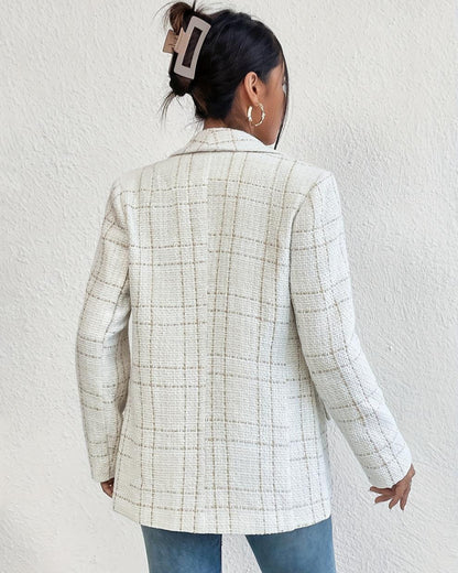 Donna di spalle con blazer a quadri bianco, fermaglio per capelli marrone, orecchini a cerchio, jeans blu. Moda autunnale elegante e casual.