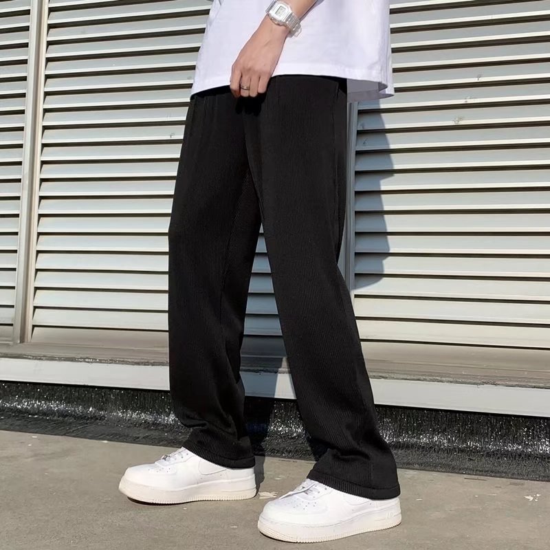Pantaloni neri larghi uomo, abbinati a scarpe da ginnastica bianche, moda casual estiva, sfondo persiane metalliche, look urbano moderno.