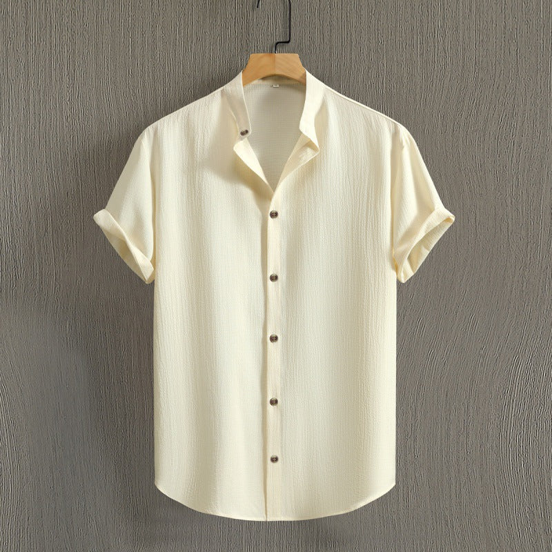 Camicia beige a maniche corte in tessuto leggero, appesa su gruccia di legno, sfondo grigio. Design casual, bottoni marroni, moda estiva uomo.