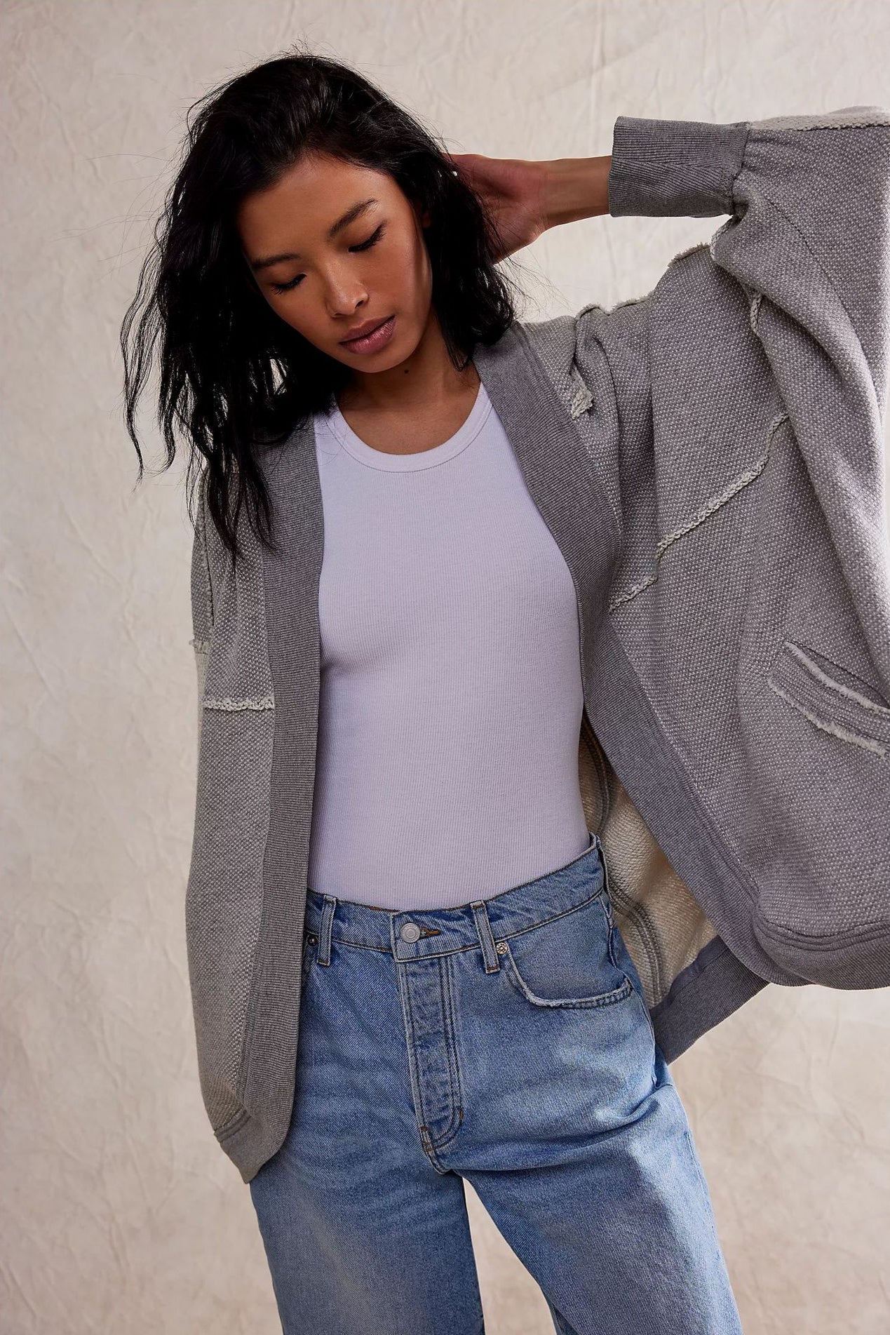 Donna con cardigan grigio e jeans, posa casual su sfondo neutro. Moda autunnale, abbigliamento casual chic, stile contemporaneo.