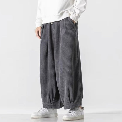 Pantaloni larghi grigi a righe verticali, indossati con felpa bianca e sneakers bianche. Moda casual uomo, stile comodo e moderno.