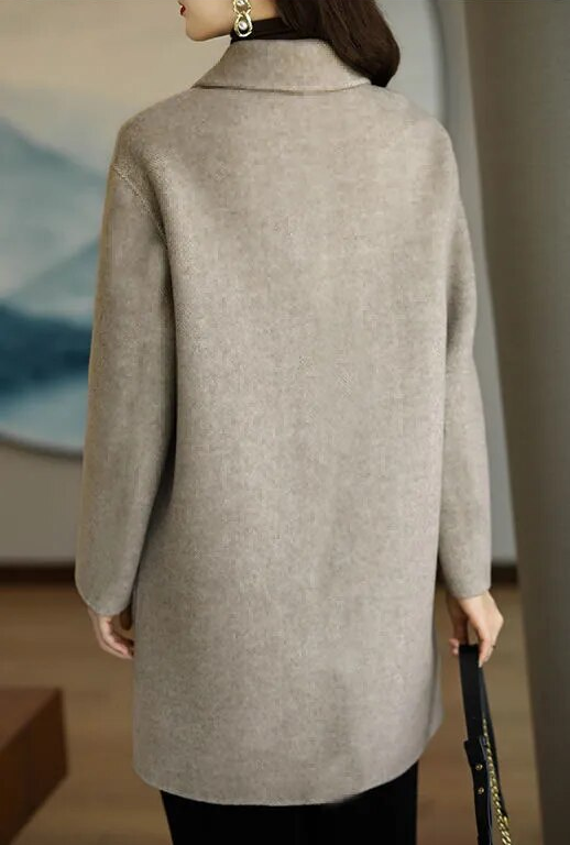 Donna con cappotto beige elegante, vista posteriore, in ambiente interno moderno. Moda autunno inverno, abbigliamento femminile chic.