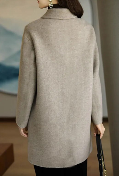 Donna con cappotto beige elegante, vista posteriore, in ambiente interno moderno. Moda autunno inverno, abbigliamento femminile chic.