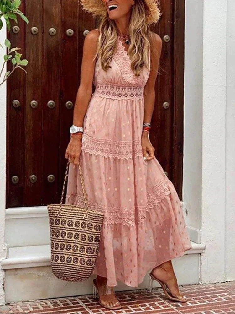 Donna con abito lungo rosa a pois, cappello di paglia e borsa intrecciata, in piedi davanti a una porta di legno. Moda estiva elegante e casual.