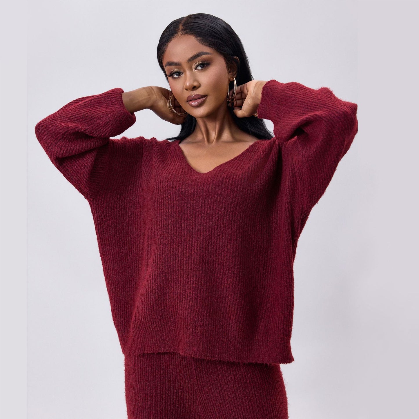 Donna con maglione rosso bordeaux, posa elegante, moda autunno inverno, abbigliamento femminile, stile casual chic, sfondo grigio chiaro.