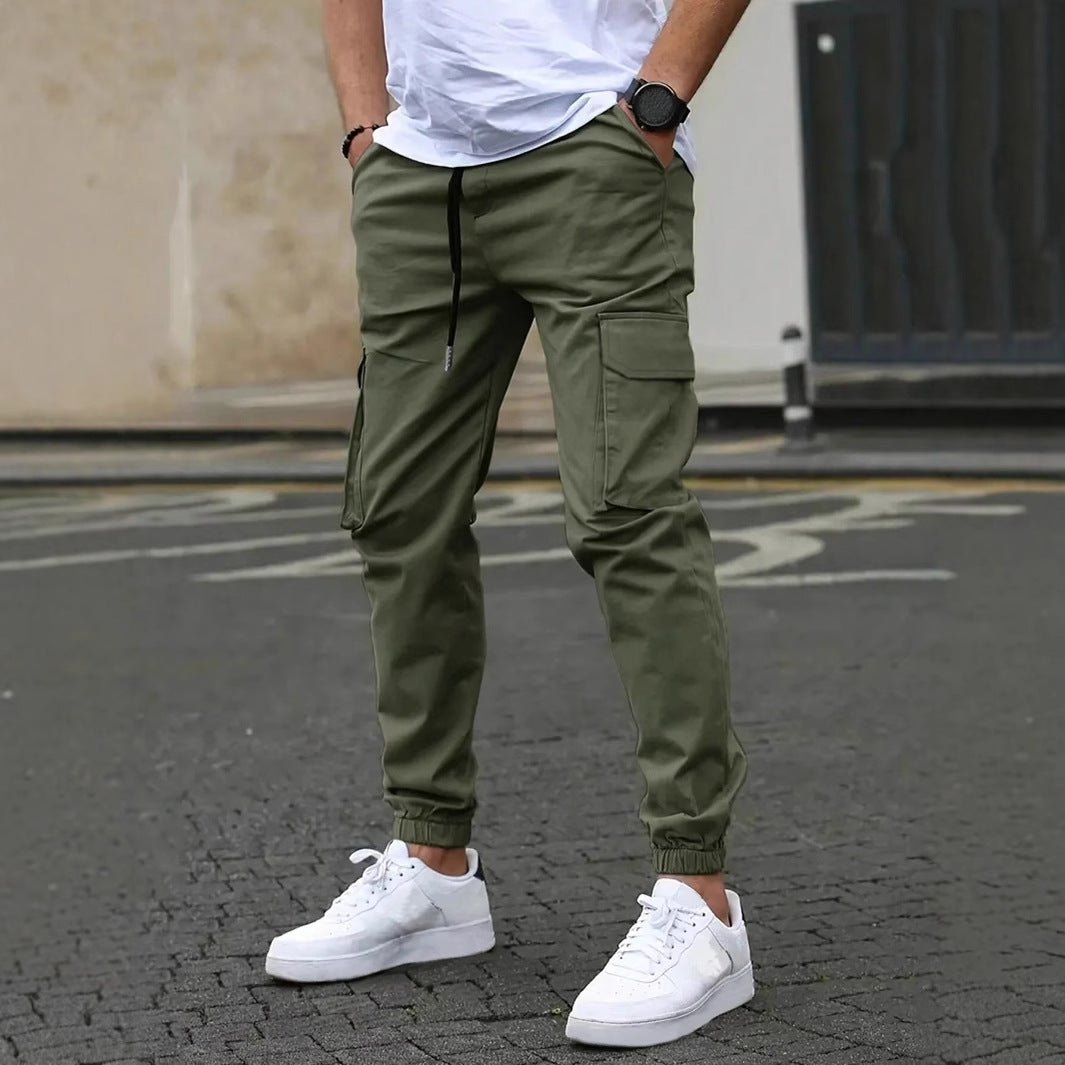 Pantaloni cargo verde oliva da uomo, stile casual, con tasche laterali, abbinati a scarpe da ginnastica bianche e t-shirt bianca.
