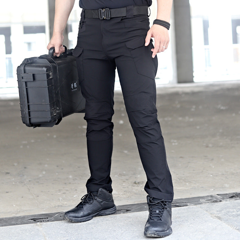 Uomo in pantaloni tattici neri con stivali, tiene una valigetta nera robusta. Abbigliamento militare, outdoor, resistente, moda uomo.