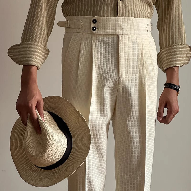 Uomo in camicia a righe e pantaloni a vita alta color crema, tiene un cappello di paglia. Moda elegante maschile, abbigliamento estivo.
