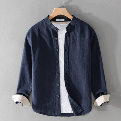 Camicia casual blu scuro da uomo con colletto alla coreana, abbinata a una t-shirt bianca, appesa su gruccia di legno. Moda maschile elegante.