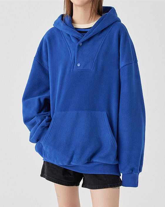Felpa blu con cappuccio, tasca frontale e bottoni, indossata con pantaloncini neri. Moda casual, abbigliamento comodo, stile urbano.