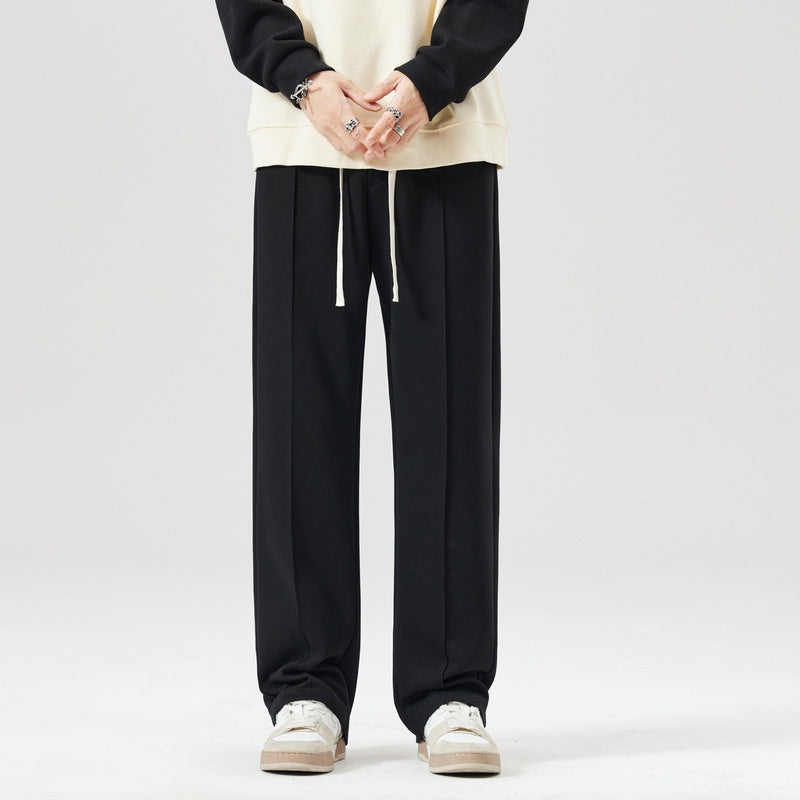Pantaloni neri larghi da uomo, stile casual, con coulisse, abbinati a felpa chiara e sneakers bianche. Moda streetwear, abbigliamento comodo.