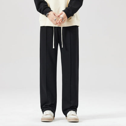 Pantaloni neri larghi da uomo, stile casual, con coulisse, abbinati a felpa chiara e sneakers bianche. Moda streetwear, abbigliamento comodo.