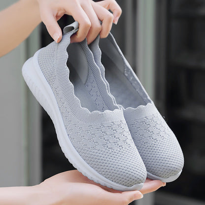Scarpe da ginnastica grigie in maglia traspirante, design slip-on, suola bianca antiscivolo, ideali per camminata e sport, comfort e stile casual.