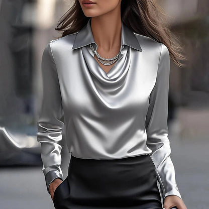 Donna con camicia di seta grigia e collana elegante, sfondo urbano sfocato. Moda femminile, abbigliamento elegante, stile sofisticato.