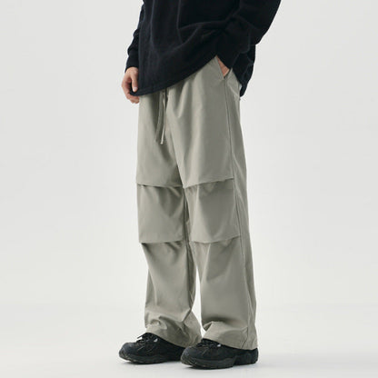Pantaloni cargo grigi da uomo, larghi e con tasche multiple, abbinati a scarpe nere e maglia scura. Stile casual e moderno.