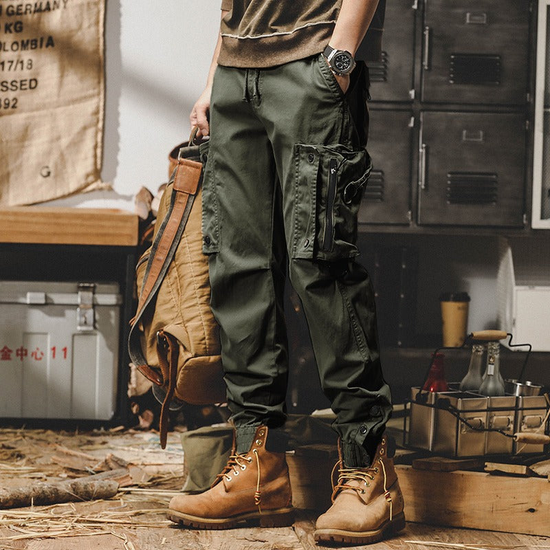 Uomo con pantaloni cargo verdi e stivali marroni, zaino in mano. Look casual e outdoor, perfetto per avventure e escursioni.