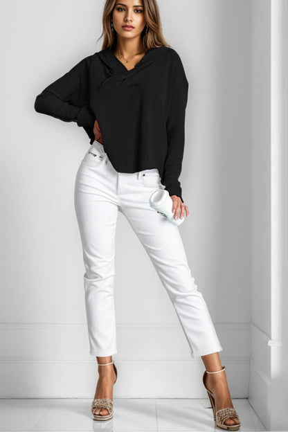 Donna in posa con maglione nero e jeans bianchi, tiene una tazza. Moda casual elegante, scarpe con tacco beige. Outfit autunnale chic.