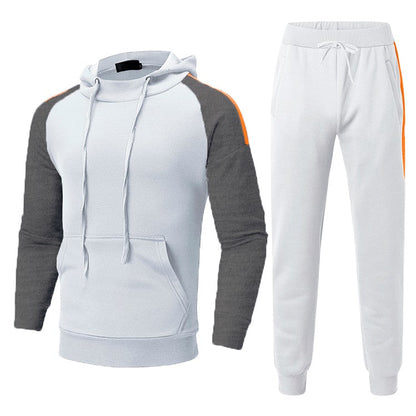 Tuta sportiva bianca e grigia con cappuccio, maniche a contrasto e dettagli arancioni. Completo casual per uomo, ideale per palestra e tempo libero.
