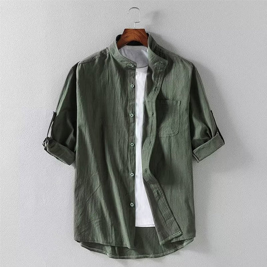 Camicia verde militare da uomo con colletto alla coreana, maniche arrotolate e taschino, appesa su gruccia. Stile casual, moda maschile.