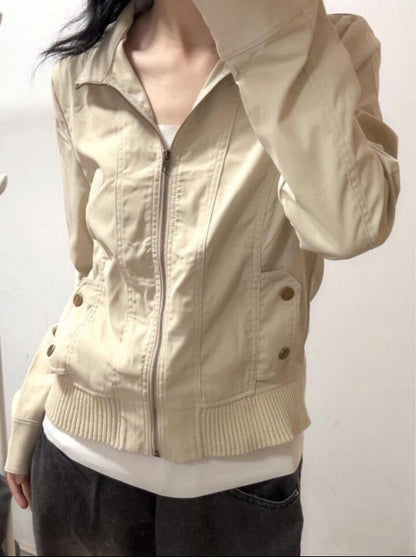 Giacca beige da donna con cerniera, tasche con bottoni, indossata sopra maglia bianca. Moda casual, abbigliamento autunnale, stile urbano.