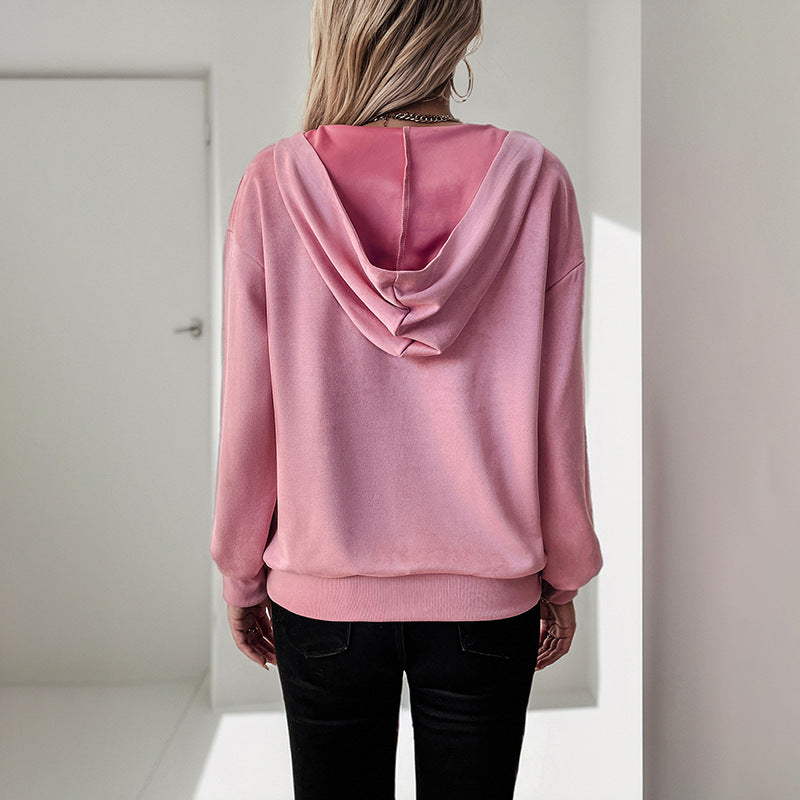 Donna di spalle con felpa rosa con cappuccio, pantaloni neri, in un ambiente minimalista. Moda casual, abbigliamento femminile, stile urbano.