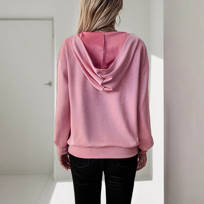 Donna di spalle con felpa rosa con cappuccio, pantaloni neri, in un ambiente minimalista. Moda casual, abbigliamento femminile, stile urbano.