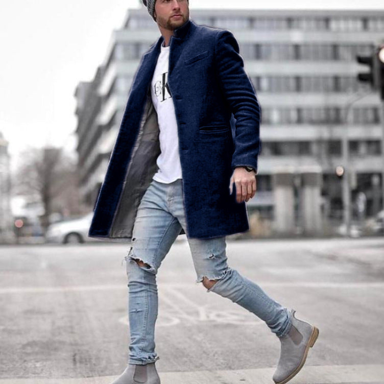 Uomo con cappotto blu scuro, jeans strappati e stivali grigi cammina in città. Moda maschile urbana, stile casual elegante.