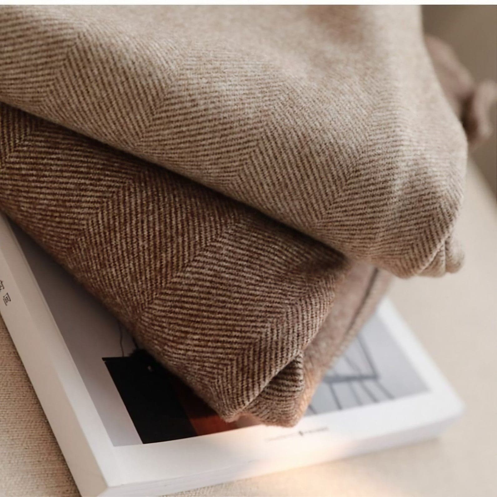 Due coperte di lana marrone a righe su un libro, tessuto morbido e caldo, ideale per arredamento casa e comfort invernale.