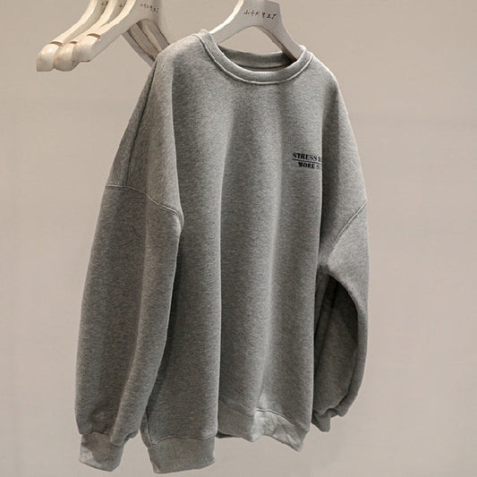 Felpa grigia oversize appesa su gruccia, con scritta "Stress Less More" sul petto. Moda casual, abbigliamento comodo, tendenza streetwear.
