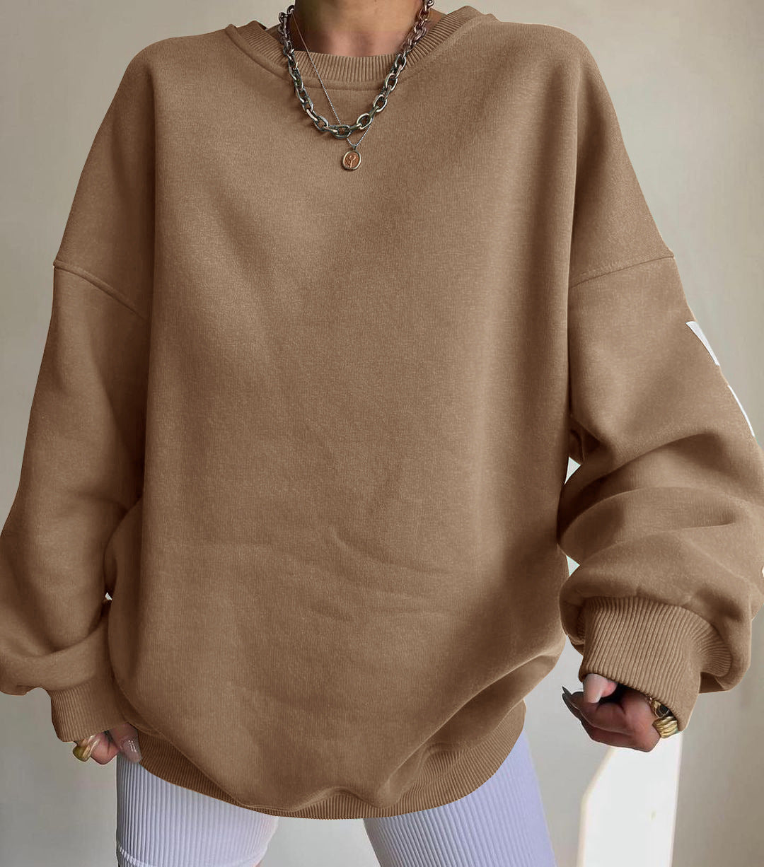 Maglione oversize marrone su persona con collana a catena, sfondo neutro. Moda casual autunno, abbigliamento comodo, stile minimalista.