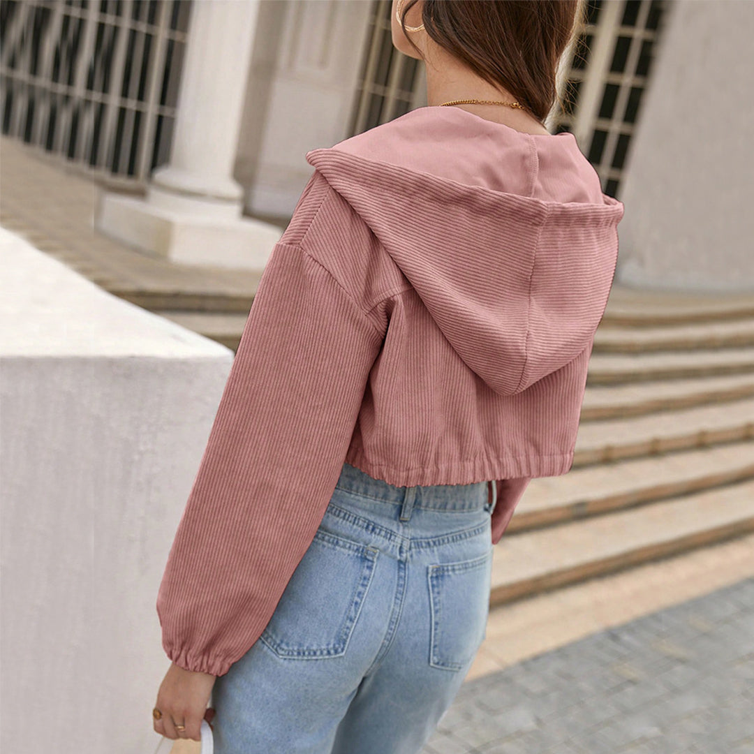 Donna di spalle con giacca corta rosa e jeans chiari, cammina su marciapiede urbano. Moda casual autunnale, giacca con cappuccio, stile giovane.