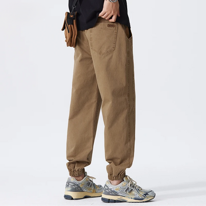 Pantaloni cargo uomo beige, stile casual, con tasche laterali e polsini elasticizzati. Scarpe da ginnastica grigie e beige. Moda streetwear.